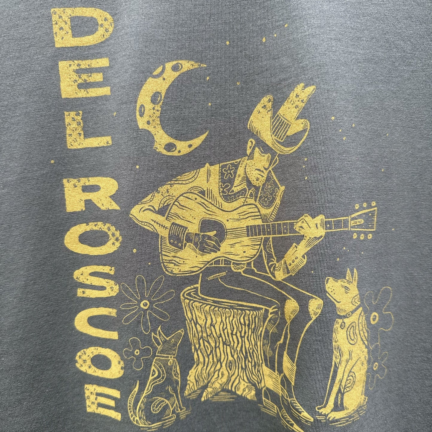 Gray t-shirt with yellow graphic of a person playing guitar, surrounded by animals and celestial elements, on a gray background.